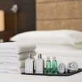 Set of free hotel amenities and white towels on the bed in hotel room. Copy space. Hotel service concept